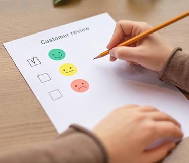 Hand filling out a customer review form with a smiley rating icon

