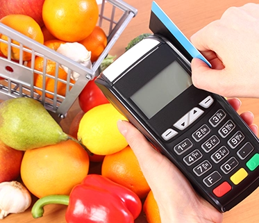 A person swiping a card on a payment terminal near fresh groceries

