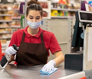 Supermarket cashier wearing a mask and gloves, cleaningthe  checkout counter


